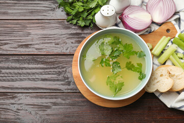 Tasty chicken bouillon in bowl, bread and ingredients on wooden table, flat lay. Space for text