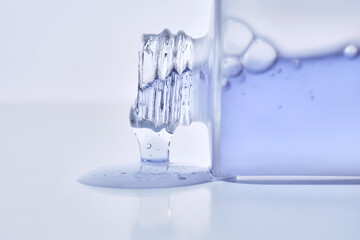 A cosmetic bottle from which a blue emulsion is poured.