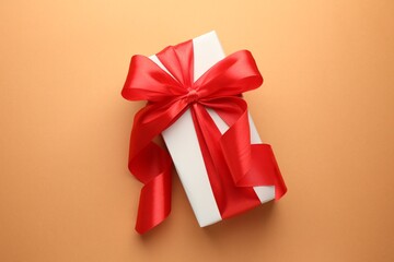 Gift box with red bow on coral background, top view