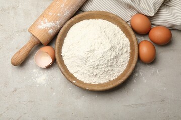 Rolling pin, flour and eggs on light grey background, flat lay
