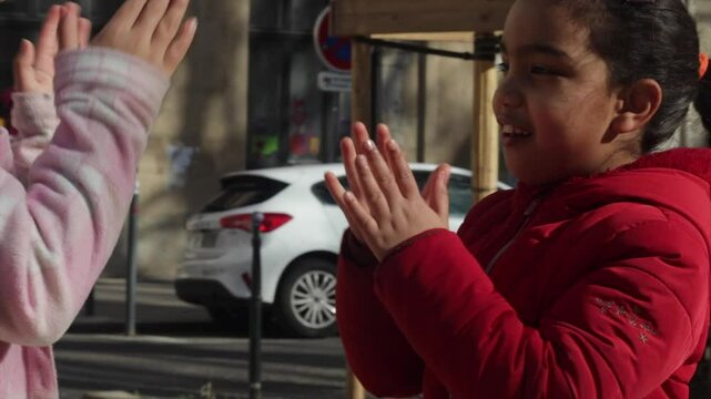 Young friends playing traditional hand clapping games, laughing together in sunlit european urban square, bonding during carefree springtime moments of childhood joy