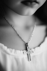 A close-up black and white photograph capturing a delicate silver cross pendant resting on the soft skin of a young child's neck. 