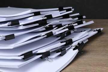 Binder clips with sheets of paper on wooden table against dark background, closeup