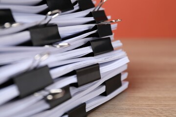 Binder clips with sheets of paper on wooden table, closeup. Space for text