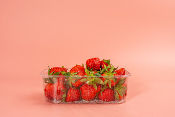 A tray of strawberries is sitting on a pink background. The strawberries are in a plastic container...