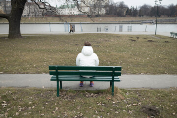 Young man sitting alone on park bench under a willow tree, looking down to the water. High quality photo © Shi 