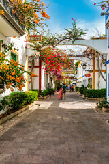 Fototapeta premium Street with blooming flowers in Puerto de Mogan, Gran Canaria, Spain. Favorite vacation place for tourists and locals on island. Puerto de Mogan with lots of bougainvillea flowers, Canary Island.