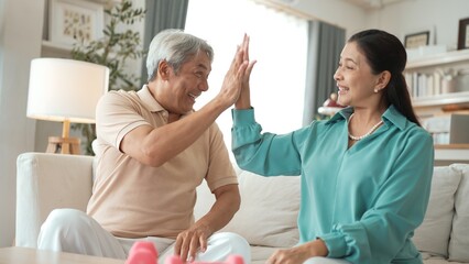 Elder woman using dumbbell at living room for boosting balance and coordination or enhancing joint...