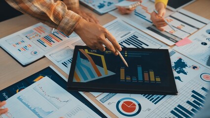 A close-up view of hands interacting with business charts and statistical data on a desk. The scene captures teamwork and analysis of performance metrics, emphasizing strategic planning. SACTR