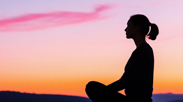 side view of a woman silhouette meditating outdoors under a colorful sunset sky, spiritual mindfulness and tranquility concept