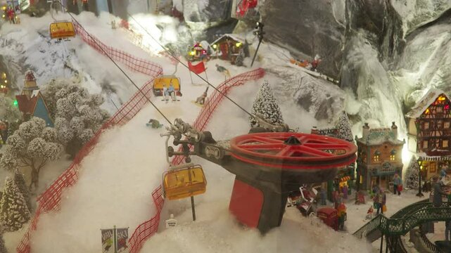 A charming miniature landscape showcases a ski resort with gondolas moving over snowy hills. Tiny skiers navigate slopes as festive decorations fill the scene, creating a magical winter atmosphere