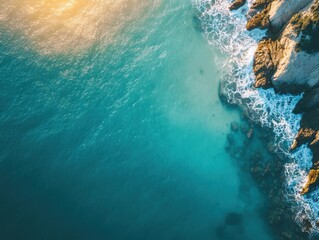 Aerial View of Turquoise Ocean Waves Crashing on Rocky Shoreline Under Bright Sunlight During Golden Hour at Coastal Location