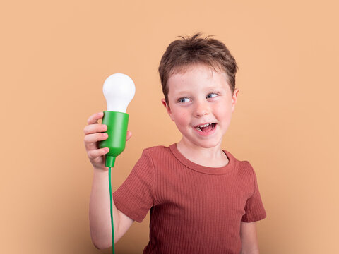 Child holding light bulb on colorful background with smile