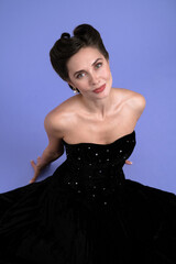 Elegant brunette woman professional model sits on the floor in black retro dress with pin-up...