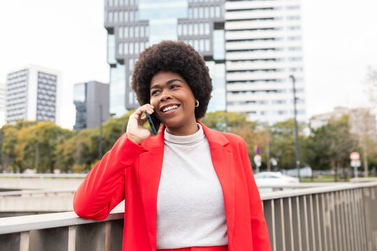 Confident woman in red jacket talking on phone in urban area