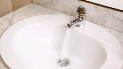 Water running from faucet into white sink in bathroom