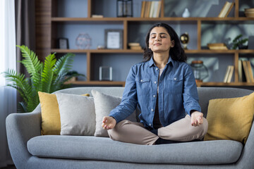 Young woman practicing meditation in a comfortable lotus pose, finding inner peace at her cozy home.