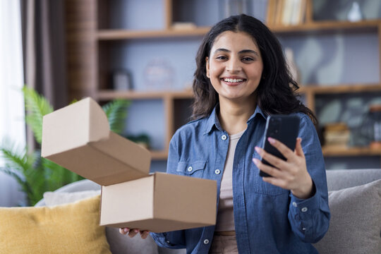 An excited woman smiles while holding her new delivery and using her phone to post about it online.
