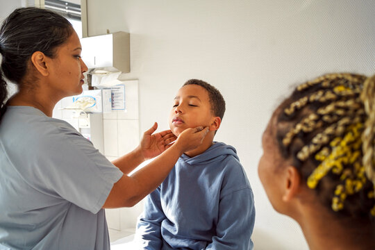 Female pediatrician checking throat of boy in medical examination room at hospital
