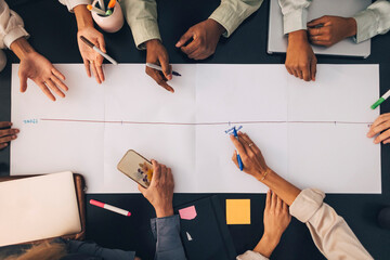 Directly above shot of multiracial male and female coworkers discussing business plan over paper kept on table at office