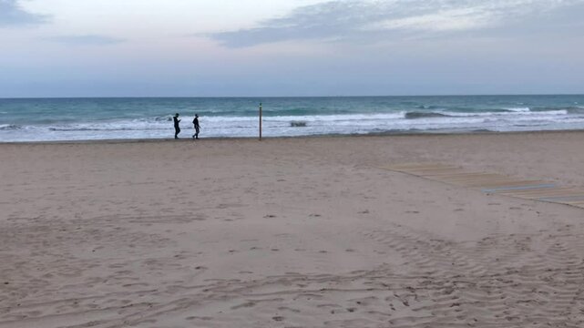 Titulo: People strolling on a wide sandy beach with ocean waves under a cloudy sky