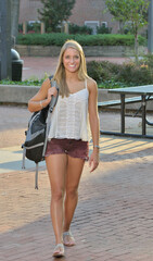 Beautiful young woman in tank top and short walks on campus with a backpack draped over one shoulder