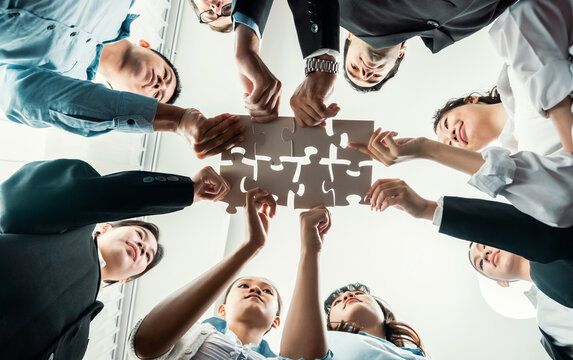 Multiethnic business people holding jigsaw pieces and merge them together as effective solution solving teamwork, shared vision and common goal combining diverse talent. Below view. Habiliment