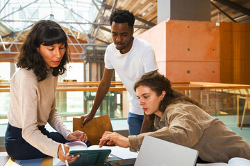 Female students discussing over digital tablet while man standing near desk in university library
