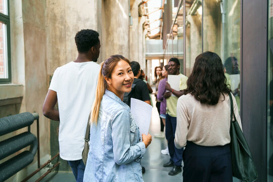 Portrait of smiling female student looking back while walking with friends in college corridor