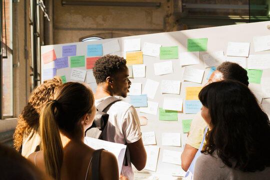 Multiracial male and female students searching on bulletin board in university campus