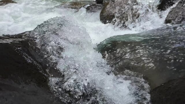 River water crashing on rock in slow motion,  camera tracks forwards into the breaking white foam. In slow motion.