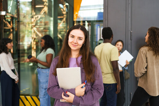 Portrait of smiling female student with assignment standing at college campus