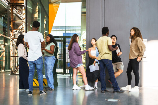 Full length of multiracial students discussing while standing in college campus