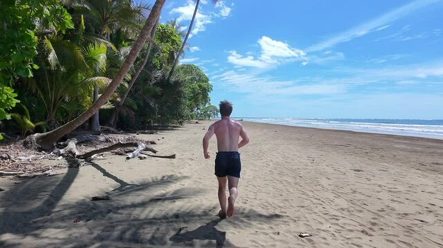 Athletic man runs along pacific coast beach in Costa Rica, Camera follows behind