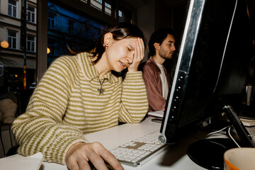 Sad female computer programmer with head in hand sitting at desk