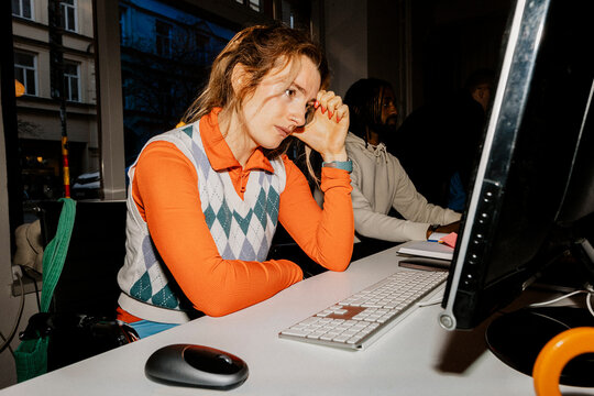 Worried female entrepreneur leaning on elbow and looking at computer screen