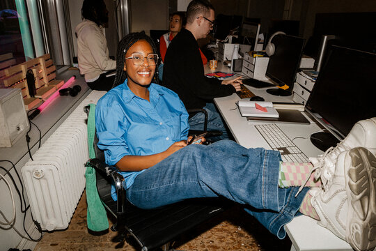 Portrait of smiling female entrepreneur sitting with feet up on table at office