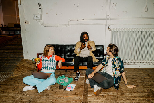 Male entrepreneur sitting on sofa and talking with colleagues at office