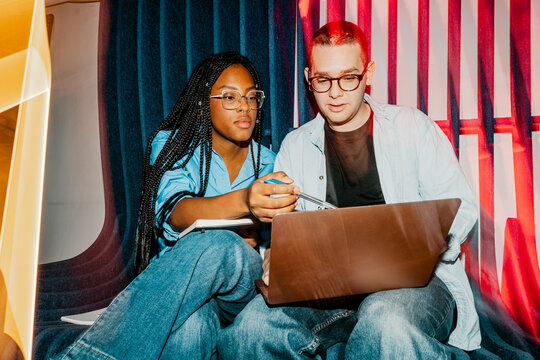 Female business professional assisting male colleague using laptop at office
