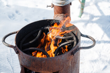 An old, rusty pot releases bright flames from its opening, contrasting sharply with the soft,...