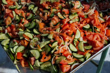 A large metal tray that is filled with fresh tomatoes, crisp cucumbers, and pungent onions, creating a vibrant assortment of ingredients perfect for salads and various dishes