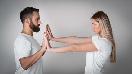 Resistance to tyranny. Woman repels with hands man claiming to her personal space on gray background, studio shot