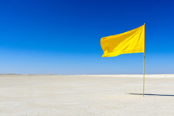Yellow Warning Flag Stands Firm in an Open, Barren Landscape Under a Clear Blue Sky During Daylight