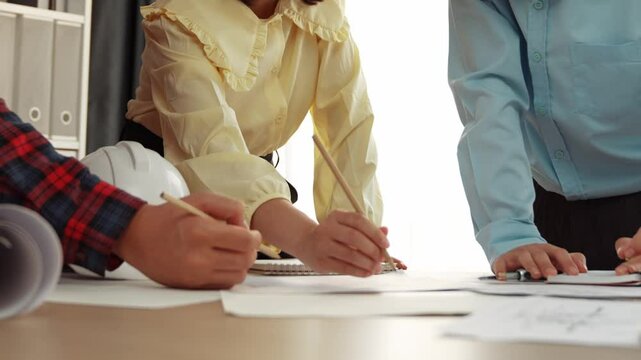 Smart architect and safety engineer discussion about building blueprint on table with architectural document, measurement tools and wooden block scatter around at modern office. Closeup. Delineation.