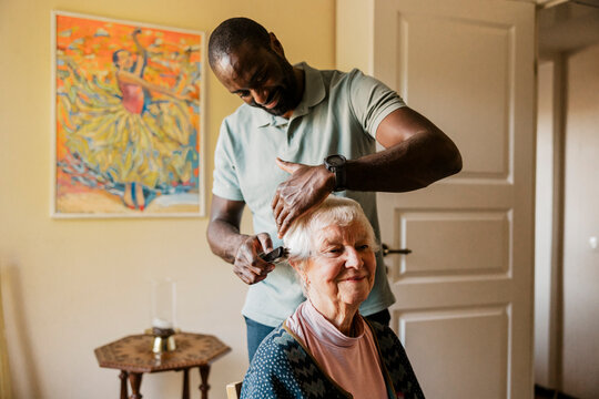 Male caregiver combing hair of smiling senior woman at home