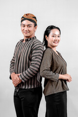 A Indonesian man and a woman stand confidently back to back, wearing traditional lurik attire, exuding pride and happiness.