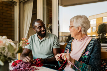 Senior woman knitting and talking with male nurse while sitting at porch