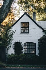 A delightful white cottage nestled amidst vibrant greenery, situated in a peaceful neighborhood that glows beautifully in the golden light of late afternoon