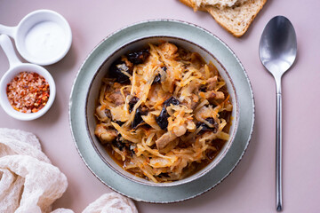 A hearty lunch for the whole family: bigus with meat and prunes in a nice plate. Stewed cabbage with meat in a plate on a gray background. View from above. Close-up