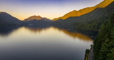 Serene Lake Crescent at sunset, reflecting mountains. Highway curves along the shore. Peaceful landscape. Port Angeles, Washington, USA